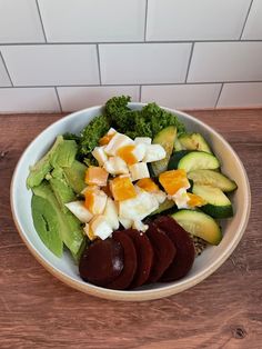 a white bowl filled with vegetables on top of a wooden table next to a tile wall