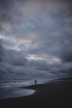 a person standing on the beach in front of some dark clouds and people walking along the shore