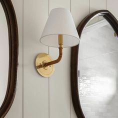 a wall light with a white shade on it next to a mirror and lamp fixture