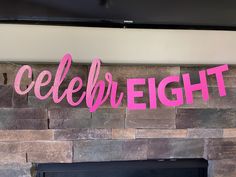 a pink sign that says celebration on the side of a brick wall next to a fireplace