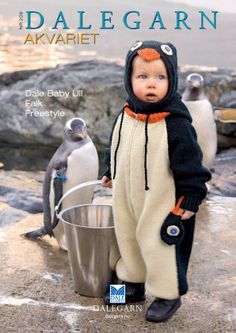 a baby doll is standing next to penguins on the rocks and holding a bucket with water in it