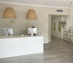 the front desk of an office with two computer screens on it's wall and wicker baskets hanging from the ceiling