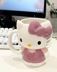 a hello kitty coffee mug sitting next to a keyboard