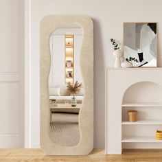 a large mirror sitting on top of a wooden floor next to a white shelf filled with vases