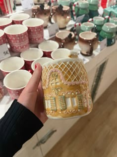 a person holding up a small cup in front of many other cups on display at a store