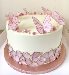 a white cake with pink butterflies on top and gold trim around the edges, sitting on a plate