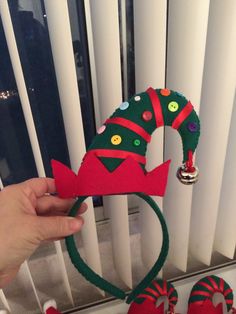 a hand holding up a green and red elf's hat next to some candy canes