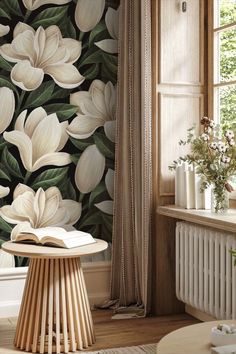 an open book on a table in front of a flowered wallpaper with white flowers