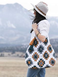 a woman carrying a crocheted bag in the desert with mountains in the background