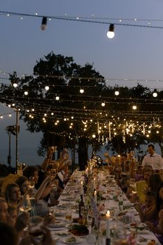 a group of people sitting around a long table with food and drinks on top of it