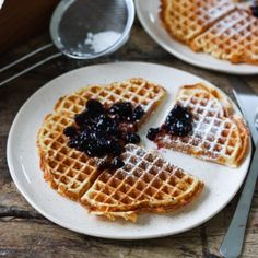 two waffles with blueberries on them are sitting on a plate next to a fork and knife