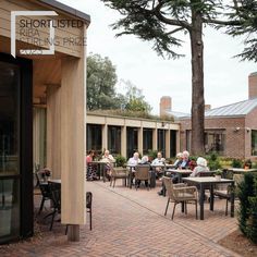 people are sitting at tables outside on the patio in front of a brick building and trees