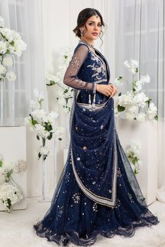 Glistening & Gleaming kamdani embellishments over midnight blue hue, a versatile floor-length gown with zardozi work on bodice finished with delicate ruffles & gota details. This look is completed with draped heavily embellished dupatta. Gown Fabric: Net & Silk Net Gown Length: 60” (customisable mention in order notes) Dupatta Fabric: Net (not stitched to outfit) Gown & Dupatta color: Midnight Blue This is a two-piece outfit including gown & Draped dupatta. All outfits are fully lined Lining in Chanderi Lehenga With Mirror Work In Maxi Length, Navratri Embellished Maxi Sharara, Embellished Maxi Length Sharara For Navratri, Embellished Sharara For Navratri In Maxi Length, Evening Anarkali Pre-draped Saree For Eid, Anarkali Style Pre-draped Saree For Eid Evening, Blue Hand Embellished Pre-draped Saree For Festive Occasions, Eid Anarkali Set For Reception With Traditional Drape, Eid Reception Anarkali Set With Traditional Drape