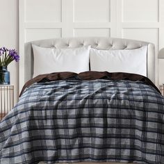 a bed with white pillows and blue plaid comforter on it in front of a wall