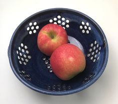 two apples in a blue bowl on a white table