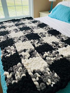 a large black and white crocheted blanket on top of a bed next to a window