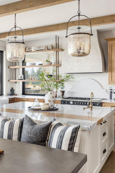 a large kitchen with an island and two hanging lights over the stove top, in front of a window