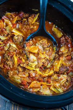 a crock pot filled with cabbage and meat stew on top of a wooden table