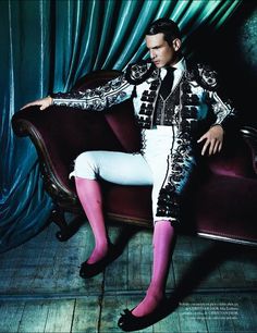 a man sitting on top of a purple couch in front of a blue curtain with pink socks