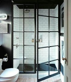 a white toilet sitting next to a shower in a bathroom under a window with glass doors