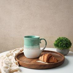 a cup and croissants on a wooden tray next to a potted plant