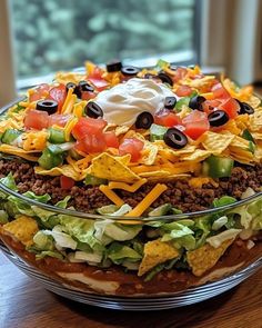 a large bowl filled with taco salad on top of a wooden table