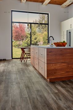 a kitchen with wood flooring and white cabinets in the background, an open window looks out onto a yard