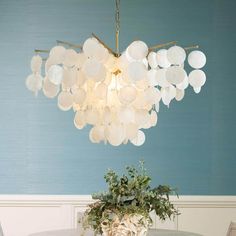 a chandelier hanging over a dining room table with plates and flowers on it