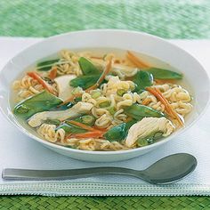 a white bowl filled with noodles and vegetables on top of a green place mat next to a spoon