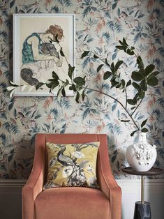 an orange chair in front of a floral wallpaper with a plant on the side