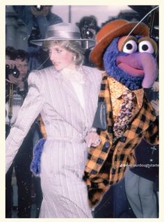 a woman in a suit and hat walking next to a man dressed up as the muppet