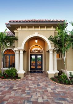 an entrance to a home with palm trees and brick pavers walkway leading into the front door