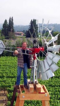 a man standing next to a windmill on top of a wooden platform in a field