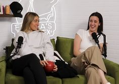 two women sitting on a green couch with microphones in front of them and one holding a red ball