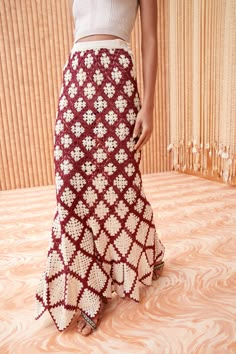 a woman in a white crop top and maroon patterned skirt standing on a wooden floor