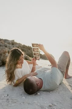 a man and woman laying on the beach reading books