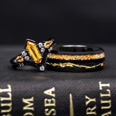 two wedding rings with yellow and white diamonds on top of each other next to a book