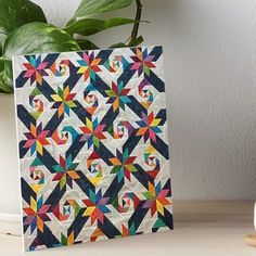 a colorful quilt is displayed on a table next to a potted plant and white vase