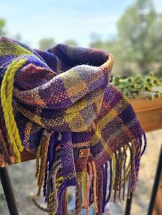 a multicolored scarf is hanging on a wooden bench outside with trees in the background