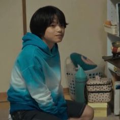 a young man sitting on the floor in front of a bookshelf