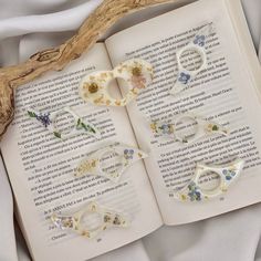 an open book with flowers on it and some scissors laying next to each other in front of a branch