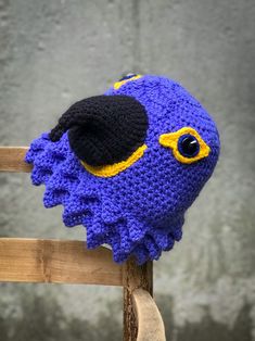 a blue crocheted hat with an eyeball on it sitting on top of a wooden chair