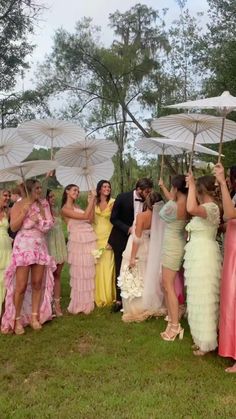 a group of people standing around each other holding umbrellas in the grass with trees in the background