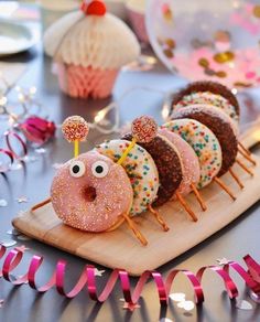 there are donuts with sprinkles and eyes on the wooden board next to pink streamers