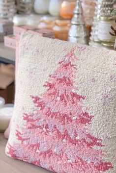 a pink and white christmas tree pillow sitting on top of a table next to candles