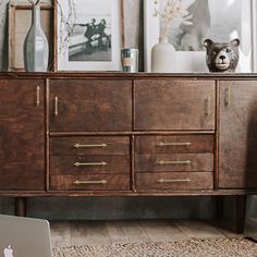 an apple laptop sitting on top of a wooden dresser next to a teddy bear and framed pictures