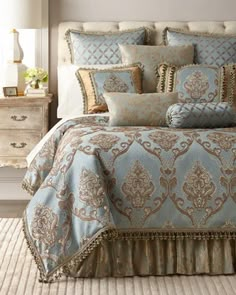 a bed with blue and gold comforters in a bedroom next to a dresser, lamp and window