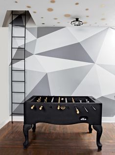 a pool table in front of a wall with geometric designs on it and a ladder to the side