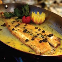 a fish dish with olives and mustard in a pan on top of a stove