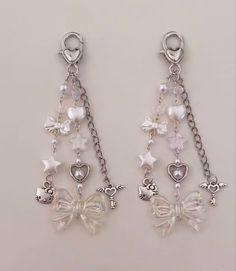 two pairs of earrings with bows, hearts and stars hanging from chains on a white surface